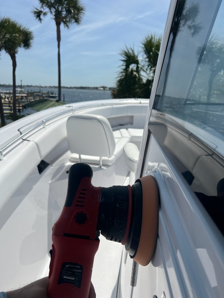 Polishing the hull of a white center console boat on the bay