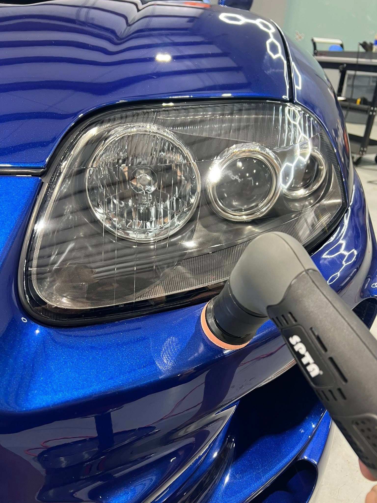 Machine polishing the front end of a metallic blue sports car to a mirror finish